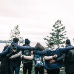 Stock photo featuring a group of friends standing beside each other, hugging, with their back to the camera