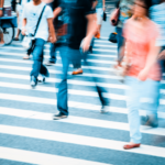 A blurred image of a crowd of pedestrians crossing a sidewalk