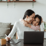 Mother working at computer with child giving her a hug